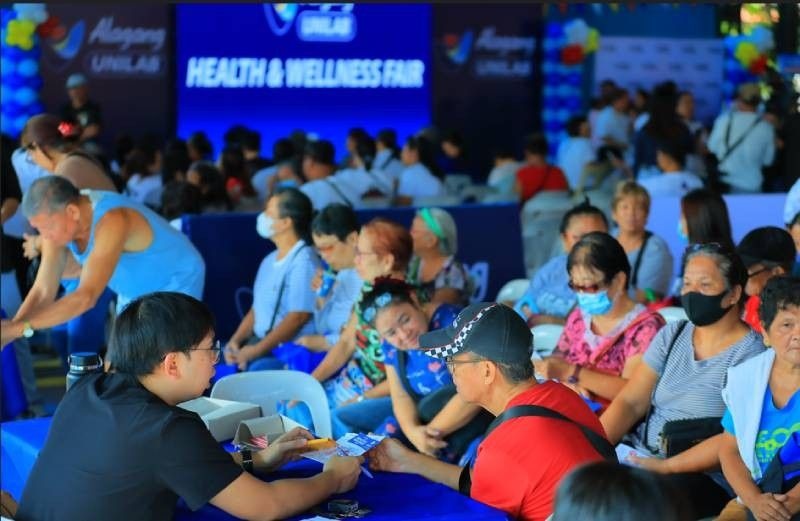 Alagang Unilab Health Community health event with attendees seated, banners reading "Alagang Unilab," and colorful decorations in a gymnasium.