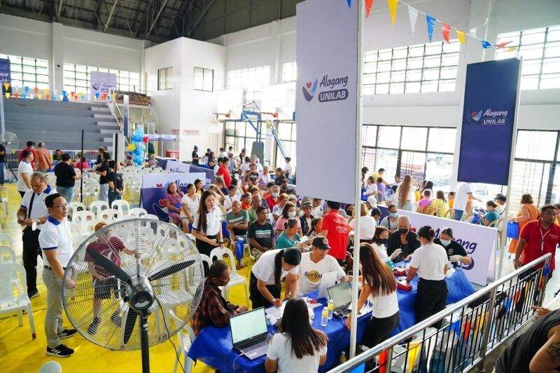 Alagang Unilab Health Community health event with attendees seated, banners reading "Alagang Unilab," and colorful decorations in a gymnasium.
