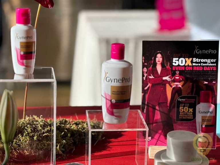 GynePro feminine hygiene product bottles displayed on clear stands, with a promotional poster highlighting its benefits, set on a red table with decorative plants